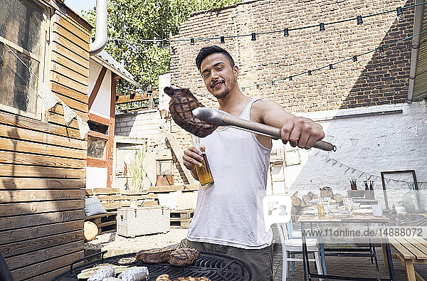 Junger Mann bereitet Fleisch auf einem Grill im Hinterhof zu