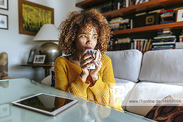 Young woman with curly hair holding mug at home