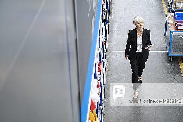 Senior businesswoman with tablet walking in a factory