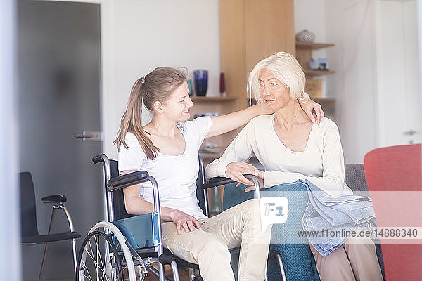 Tochter sitzt im Rollstuhl und umarmt ihre Mutter