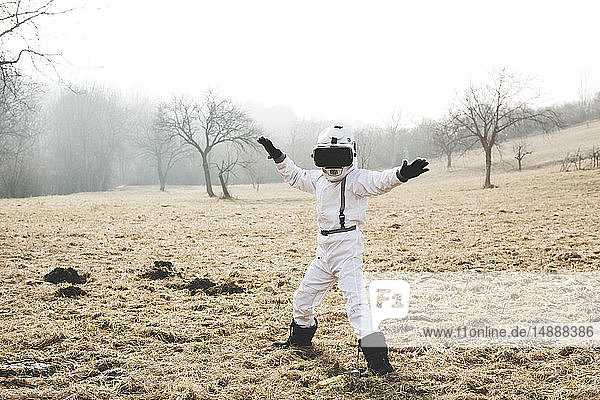 Junge im weißen Raumanzug posiert mit einer Virtual-Reality-Brille im Freien auf einer Wiese
