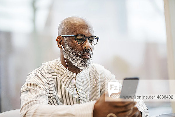 Portrait of mature businessman using smartphone and earphones