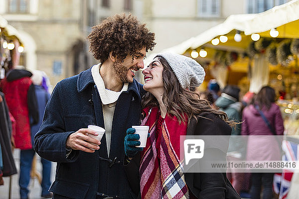 Glückliches  anhängliches junges Paar mit heißen Getränken auf dem Weihnachtsmarkt