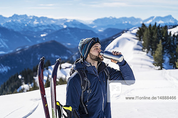 Deutschland  Bayern  Brauneck  Mann auf einer Skitour im Winter in den Bergen  der eine Pause macht und aus der Thermoskanne trinkt
