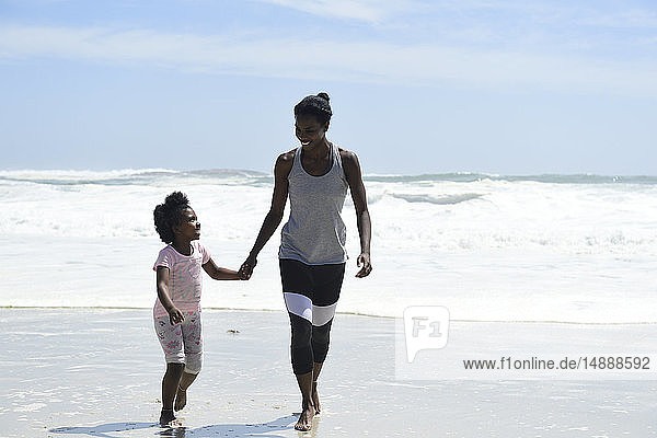 Mutter und Tochter gehen Hand in Hand am Strand