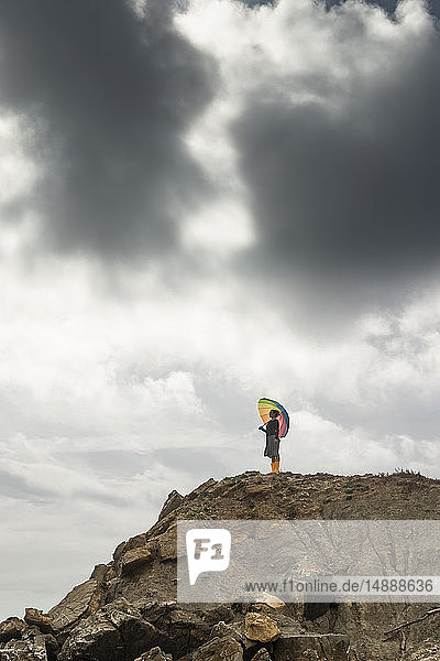 Frau mit buntem Regenschirm auf einem Hügel am Strand stehend