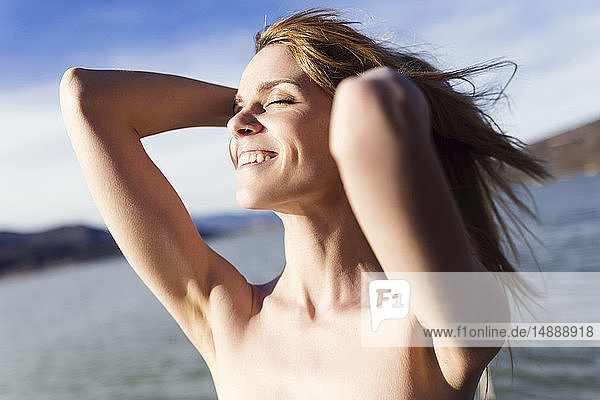 Glückliche junge Frau vor dem See  die das Sonnenlicht genießt
