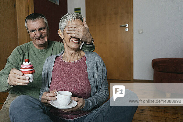 Glückliches älteres Ehepaar sitzt zu Hause auf dem Boden und amüsiert