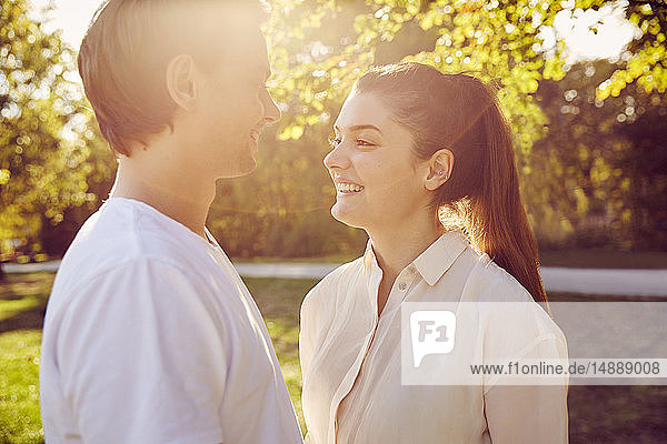 Young couple smiling at each other in a park at sunset
