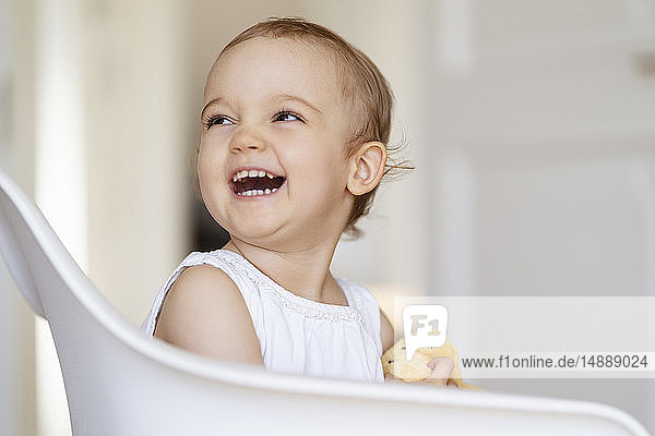 Portrait of laughing toddler girl sitting on a chair with cuddling toy