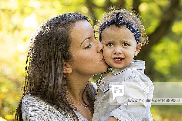 Mother kissing baby girl outdoors in autumn
