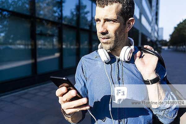 Porträt eines Mannes mit Kopfhörer  Tasche und Mobiltelefon  der in die Ferne schaut