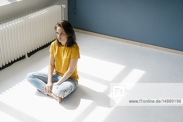 Nachdenkliche Frau sitzt im Sonnenlicht im Schneidersitz auf dem Boden