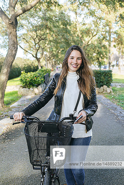 Porträt einer lächelnden jungen Frau mit Fahrrad im Park