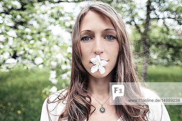 Porträt einer jungen Frau mit Apfelblüte im Mund