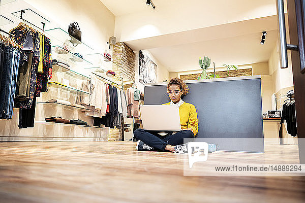 Junge Frau arbeitet in einem Modegeschäft und benutzt einen Laptop