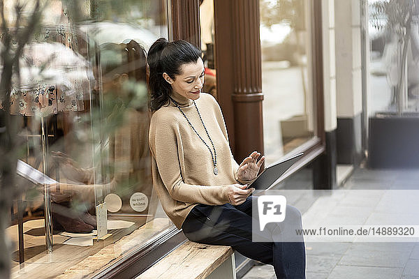 Mature woman sitting in front of her fashion store  using tablet