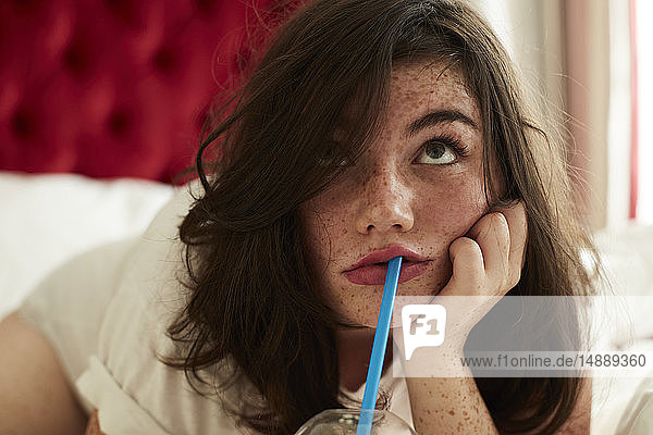 Porträt eines gelangweilten Teenagers  der mit einem Erfrischungsgetränk im Bett liegt
