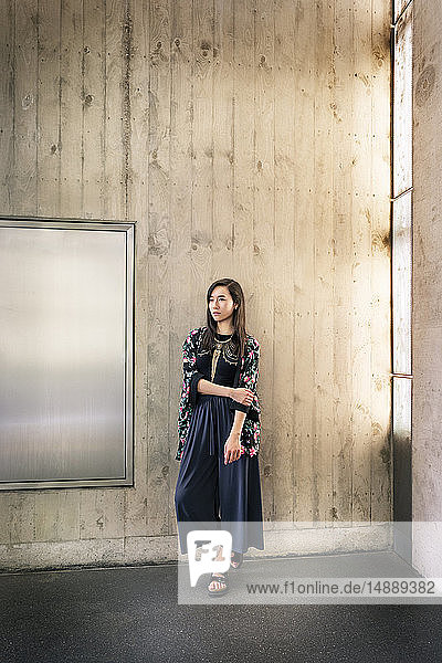 Portrait of fashionable young woman standing in front of concrete wall