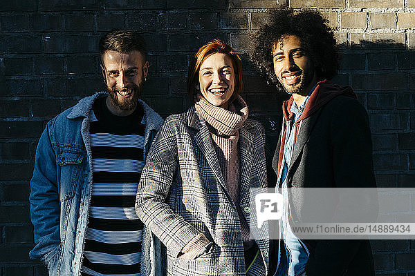 Porträt von drei glücklichen Freunden im Schatten an einer Ziegelmauer