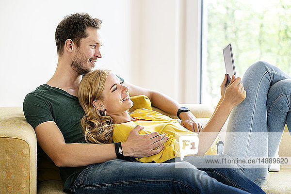 Paar  das in seinem neuen Zuhause auf der Couch sitzt und ein digitales Tablet benutzt