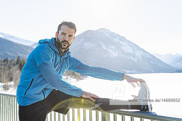 Deutschland  Bayern  sportlicher Mann streckt sich im Winter auf dem Brückengeländer