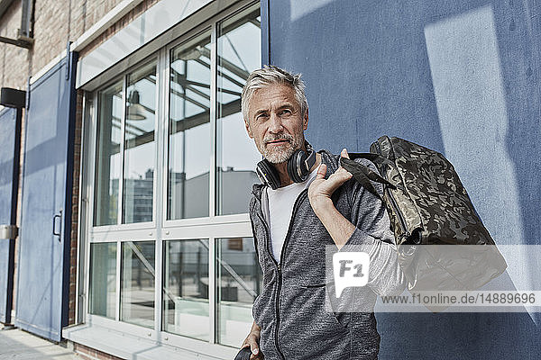 Portrait of mature man with headphones and camouflage sports bag in front of gym
