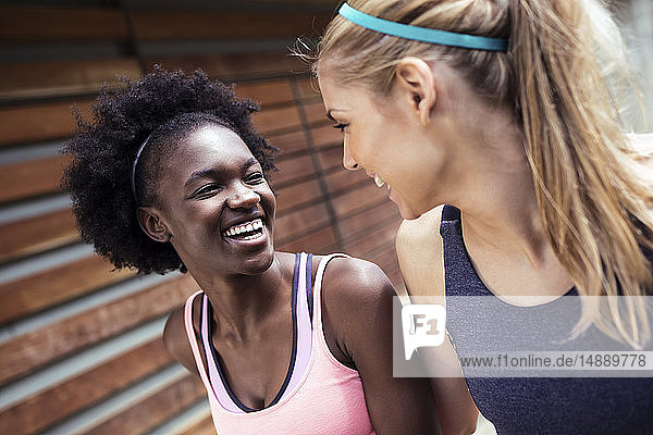 Zwei sportliche junge Frauen unterhalten sich und entspannen sich nach dem Laufen in der Stadt