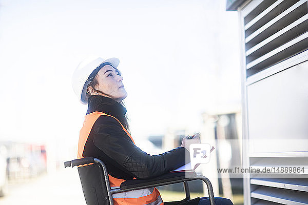 Junger Techniker mit Schutzhelm und Weste im Rollstuhl bei der Arbeit im Freien