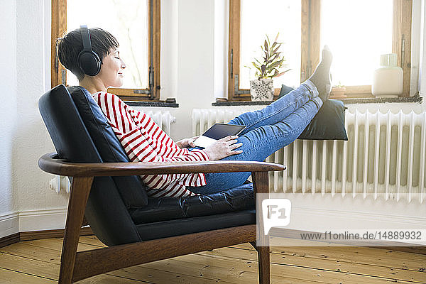 Kurzhaarige Frau mit Kopfhörern entspannt sich in Lounge Chair in stilvoller Wohnung