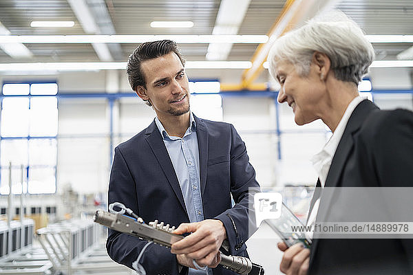 Lächelnder Geschäftsmann und leitende Geschäftsfrau bei der Untersuchung eines Werkstücks in einer Fabrik