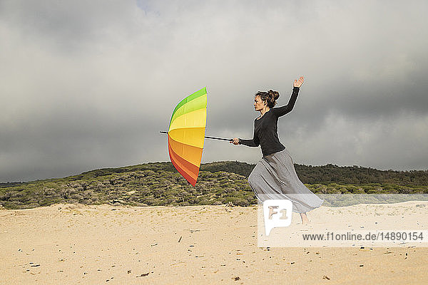 Frau hält bunten Regenschirm auf einer Düne
