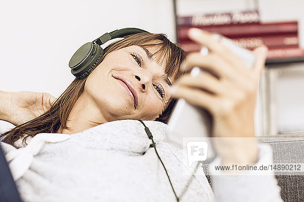 Frau liegt auf einer Couch und hört Musik mit Kopfhörern
