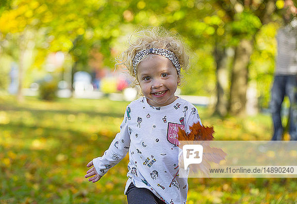 Happy little girl running with autumnal leaf in park