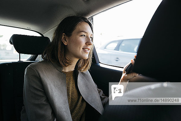 Lächelnde Frau sitzt auf dem Rücksitz eines Autos und hält ein Handy
