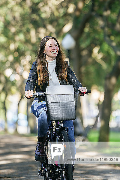 Lächelnde junge Frau fährt Fahrrad im Park