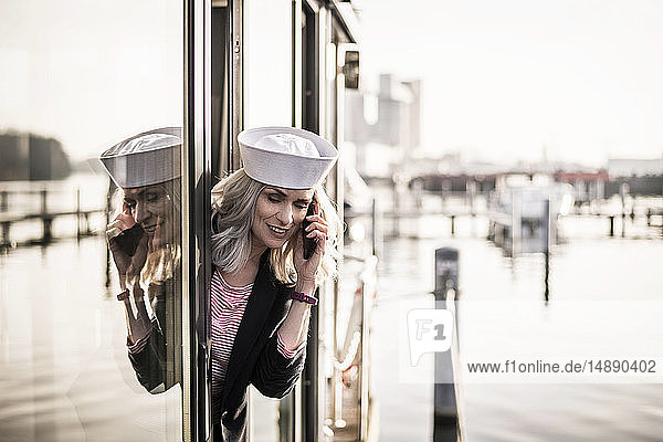 Geschäftsfrau mit Matrosenhut  auf einem Hausboot arbeitend  mit Smartphone