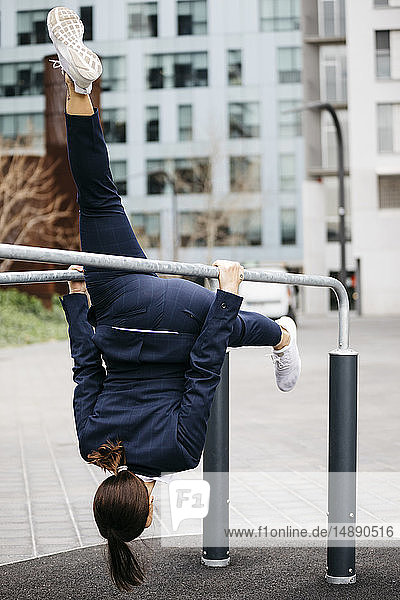 Active businesswoman doing gymnastics exercises on bars in the city