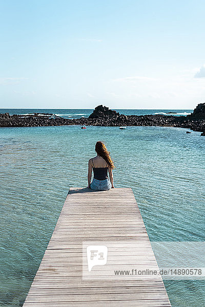 Spanien  Kanarische Inseln  Fuerteventura  Frau sitzt auf einem Steg am Meer