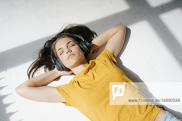 Frau liegt auf dem Boden  entspannt sich im Sonnenlicht und hört Musik