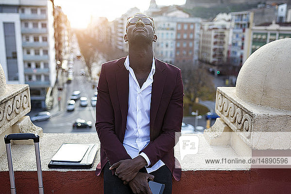 Junger Unternehmer  der auf der Hotelterrasse auf seine Verabredung wartet und sein Smartphone in der Hand hält