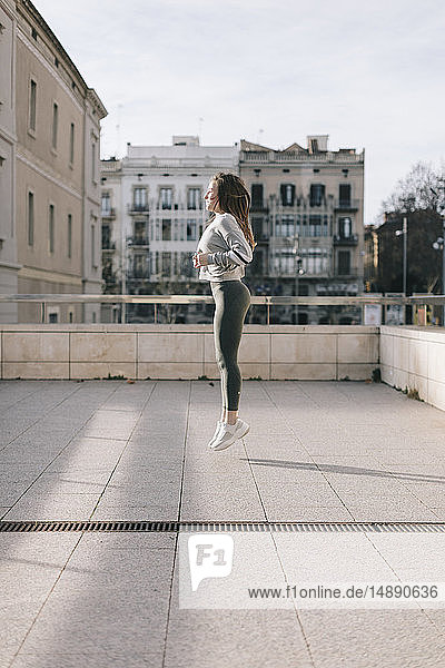 Junge Frau beim Workout auf der Terrasse springt in die Luft