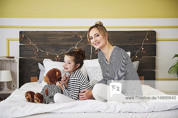 Mutter und Tochter im Bett sitzend  Mädchen mit Teddybär