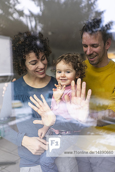 Familie schaut aus dem Fenster  Mutter trägt Tochter  berührt Glasscheibe