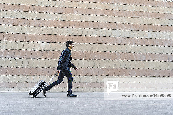 Running young businessman with rolling suitcase