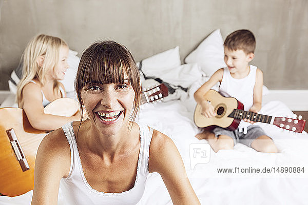 glückliche Mutter mit Kindern  die im Bett Gitarre spielen