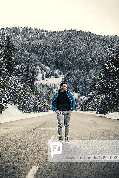 Junger Mann geht auf einer verschneiten Straße mit Bäumen im Hintergrund