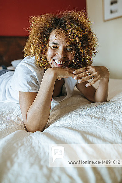 Porträt einer glücklichen jungen Frau mit lockigem Haar  die zu Hause auf dem Bett liegt