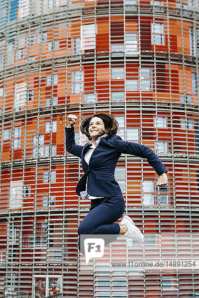 Glückliche Geschäftsfrau springt vor Bürogebäude in der Stadt