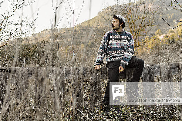 Junger Mann sitzt auf dem Zaun und schaut auf die Aussicht